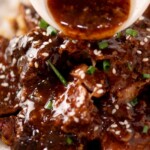 Close-up of a mouthwatering boneless beef ribs recipe made in a slow cooker, topped with savory sauce, sprinkled with sesame seeds and chopped green onions, and served over a bed of fluffy white rice. Text overlay reads slow cooker boneless beef ribs.