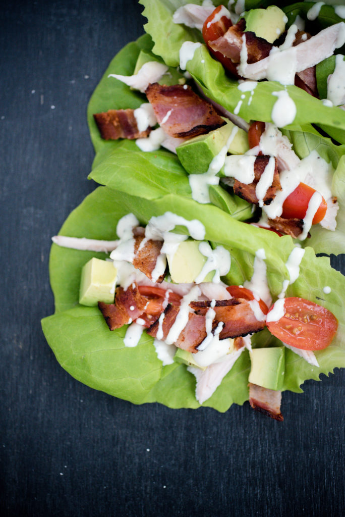 lettuce cups filled with chicken, avocado, bacon, tomato, and drizzled with ranch on a dark surface