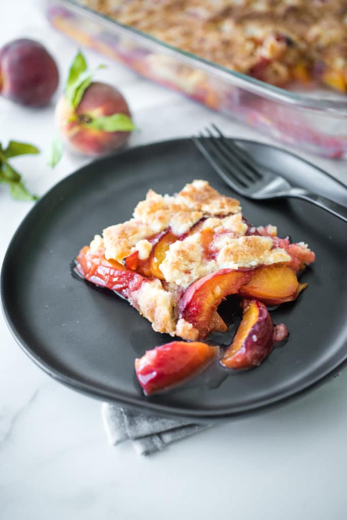 a slice of peach cobbler on a round black plate