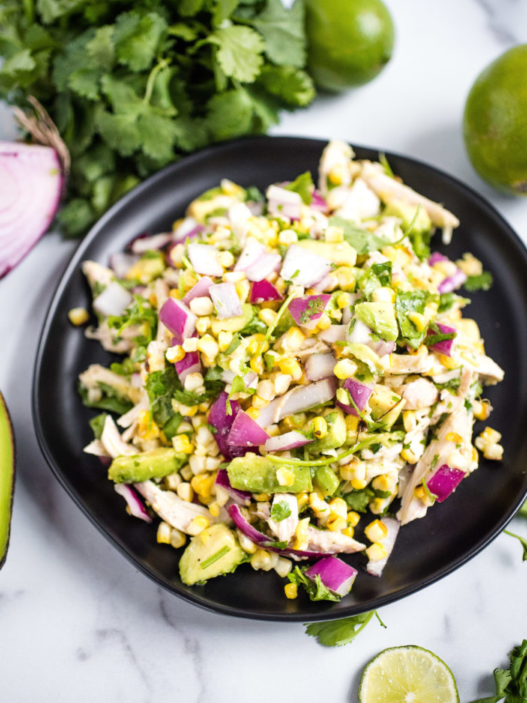 a black plate of avocado chicken chopped salad with cilantro, lime and onion in the background