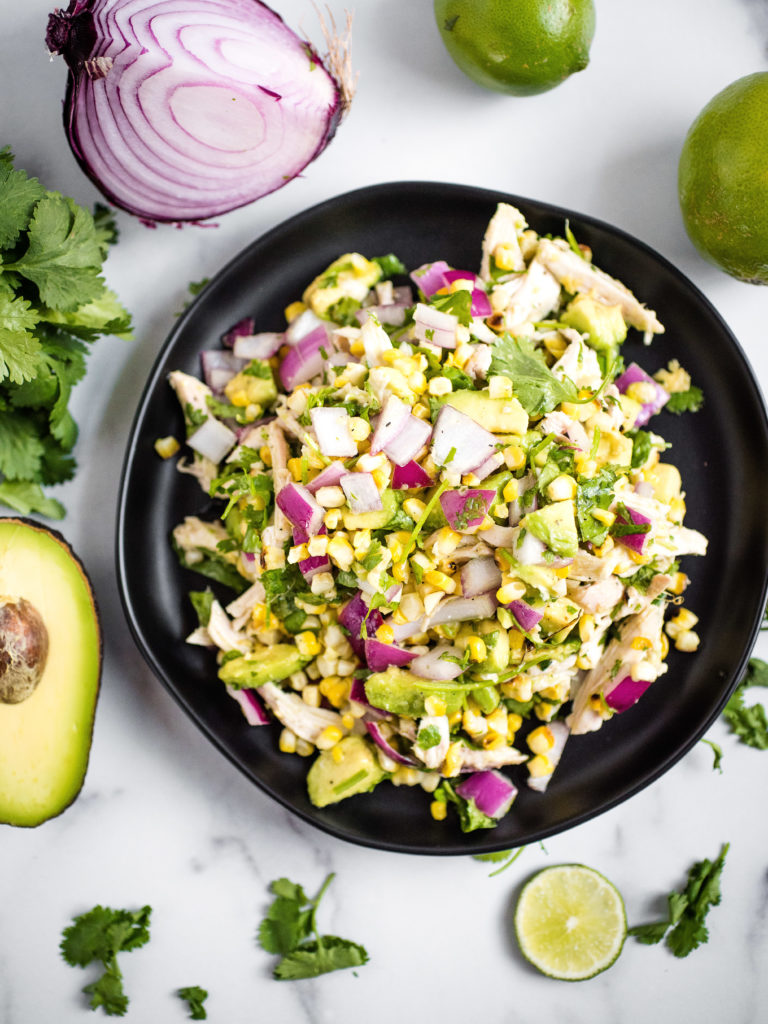 over head shot of avocado chicken chopped salad on a black plate