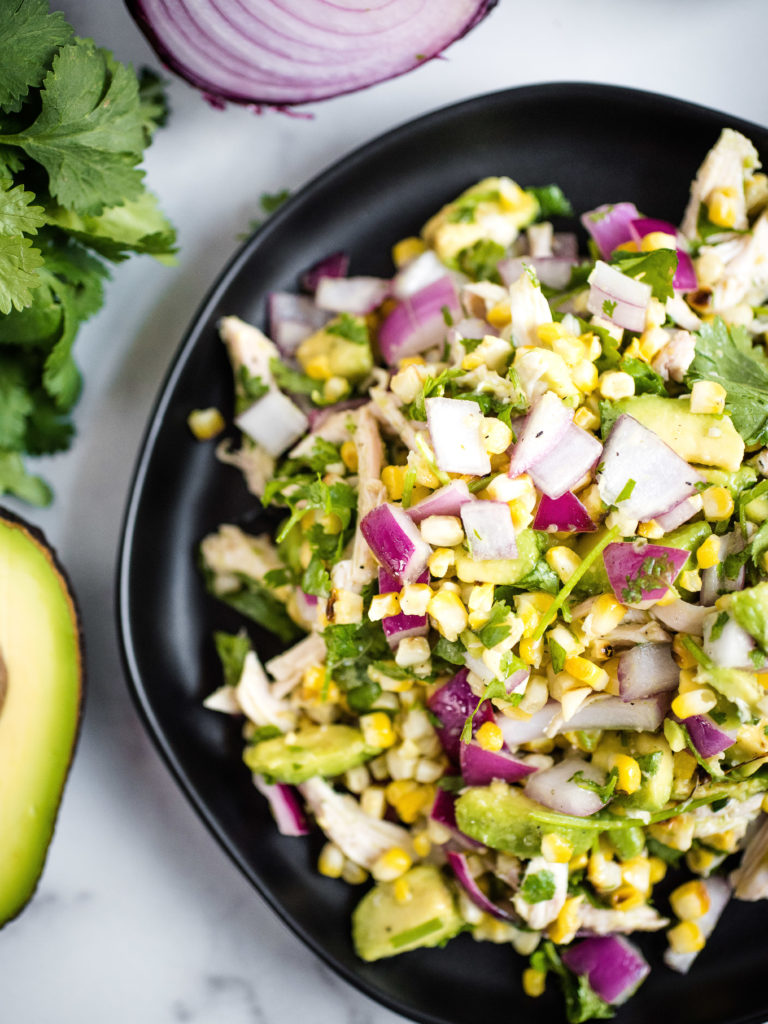 overhead shot of avocado chicken chopped salad on a black plate