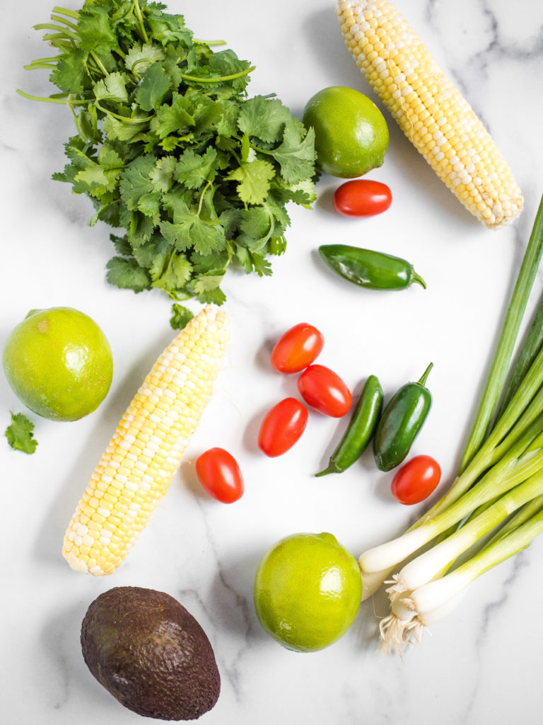 overhead shot of corn, limes, cilantro, tomatoes, jalapeno, avocado, and green onion