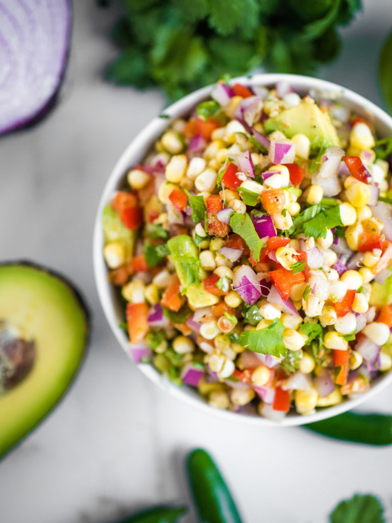 overhead shot of avocado corn salsa with cilantro, jalapeno, corn, onion, red bell pepper, and spices in a white bowl