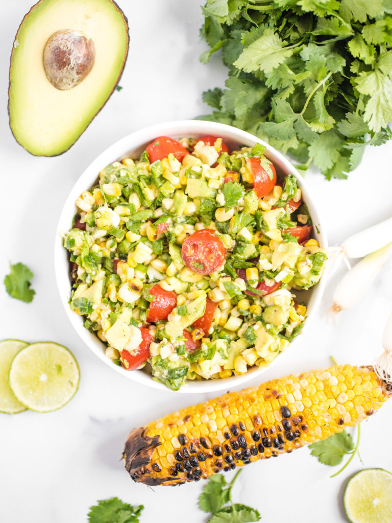 overhead shot of summer corn salad with grilled corn, avocado, cilantro, and lime on the counter around it
