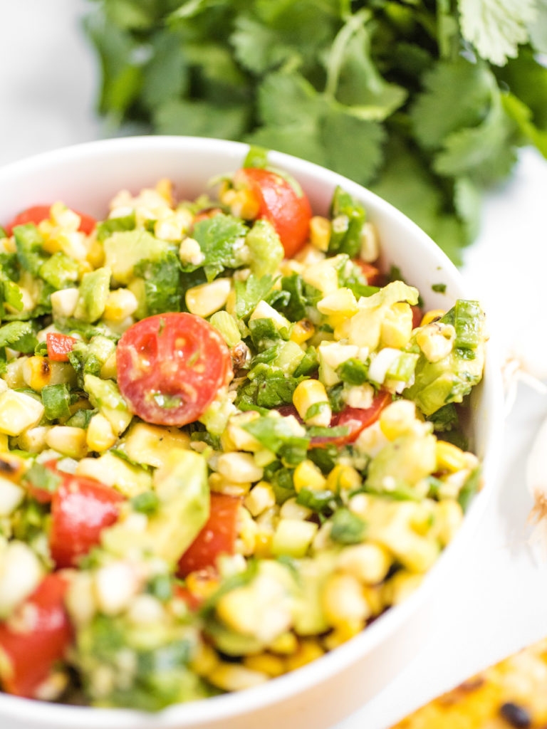 summer corn salad in a white bowl with cilantro in the background