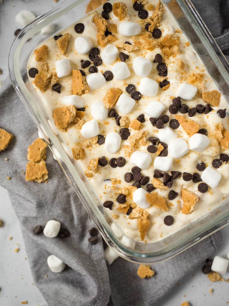 overhead shot of ice cream in a clear glass container topped with graham cracker pieces, chocolate chips, and marshmallows