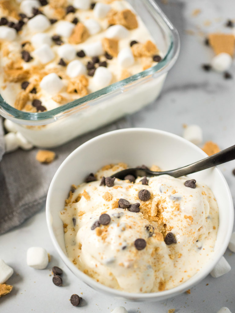 ice cream in a white bowl with the remainder of the s'mores ice cream in a glass container in the background