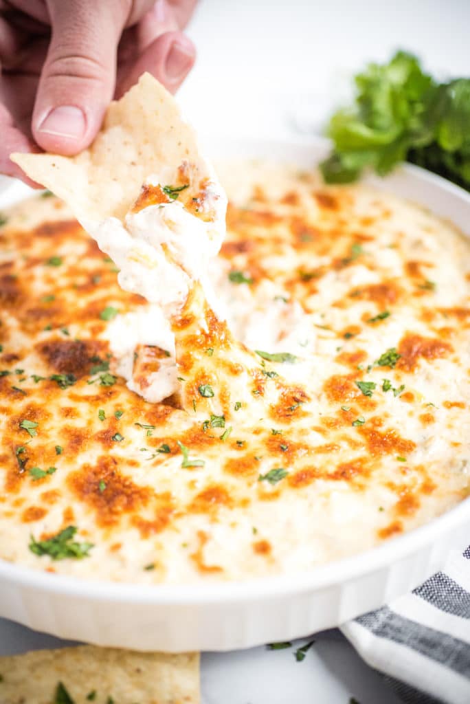 Dish of green chile queso blanco dip with hand dipping in using a tortilla chip
