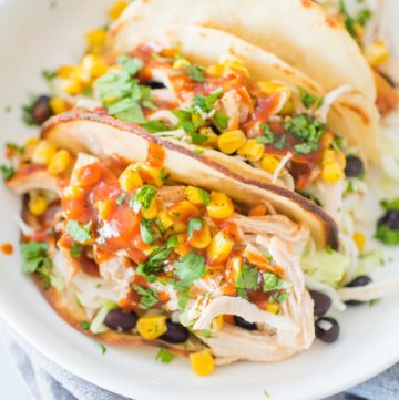 a white shallow bowl with tacos stuffed with bbq chicken, beans, corn, and cilantro