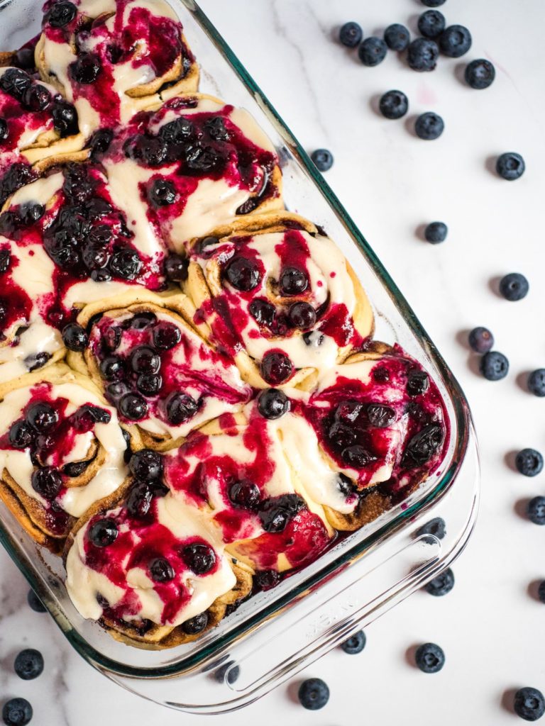 overhead shot of blueberry cinnamon rolls in a pyrex dish surrounded by blueberries