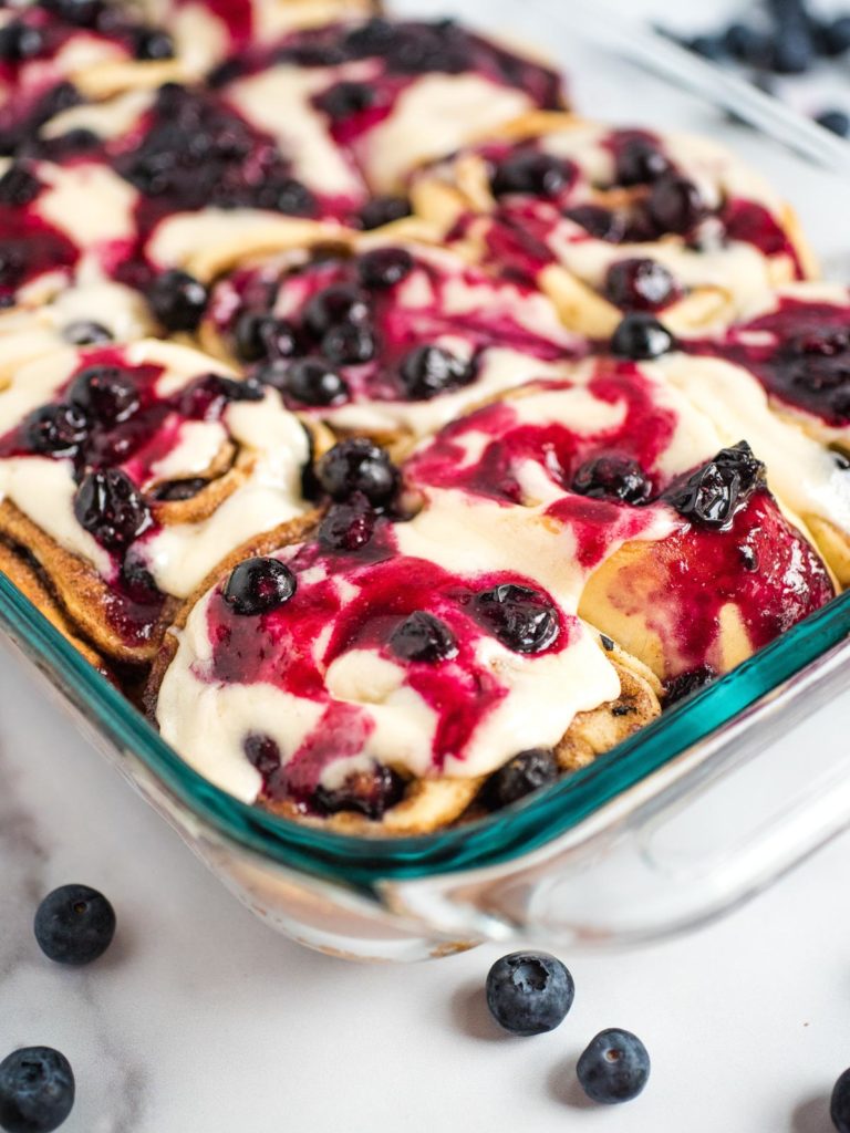 a clear pyrex dish with blueberry cinnamon rolls topped with icing and blueberries