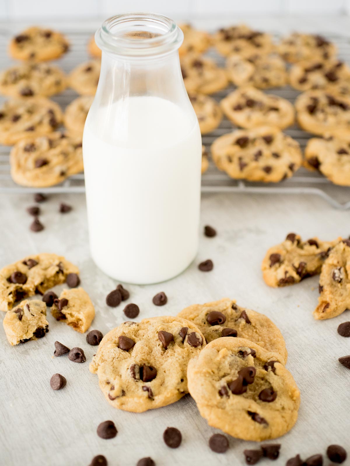 chocolate chip cookies in front of milk and a rack of cooling cookies