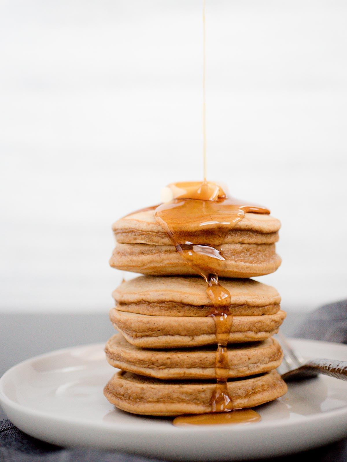 gingerbread pancakes being drizzled with syrup and topped with butter