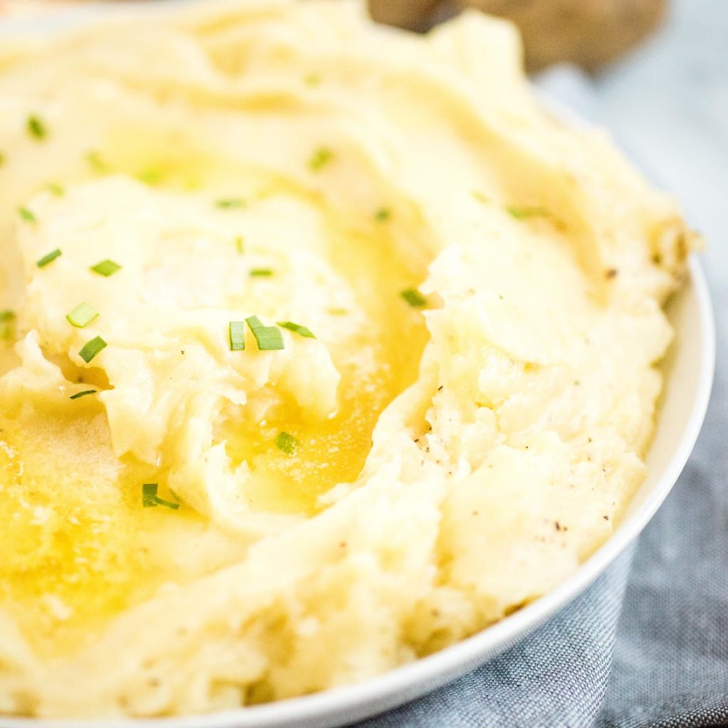 mashed potatoes in white dish topped with melted butter and chives