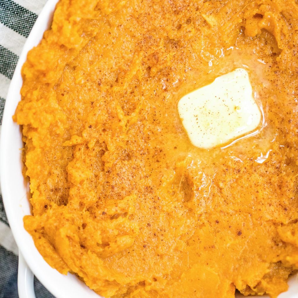mashed sweet potatoes in a white baking dish topped with butter
