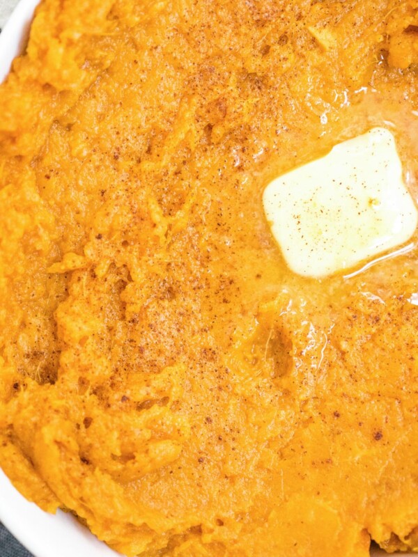 mashed sweet potatoes in a white baking dish topped with butter