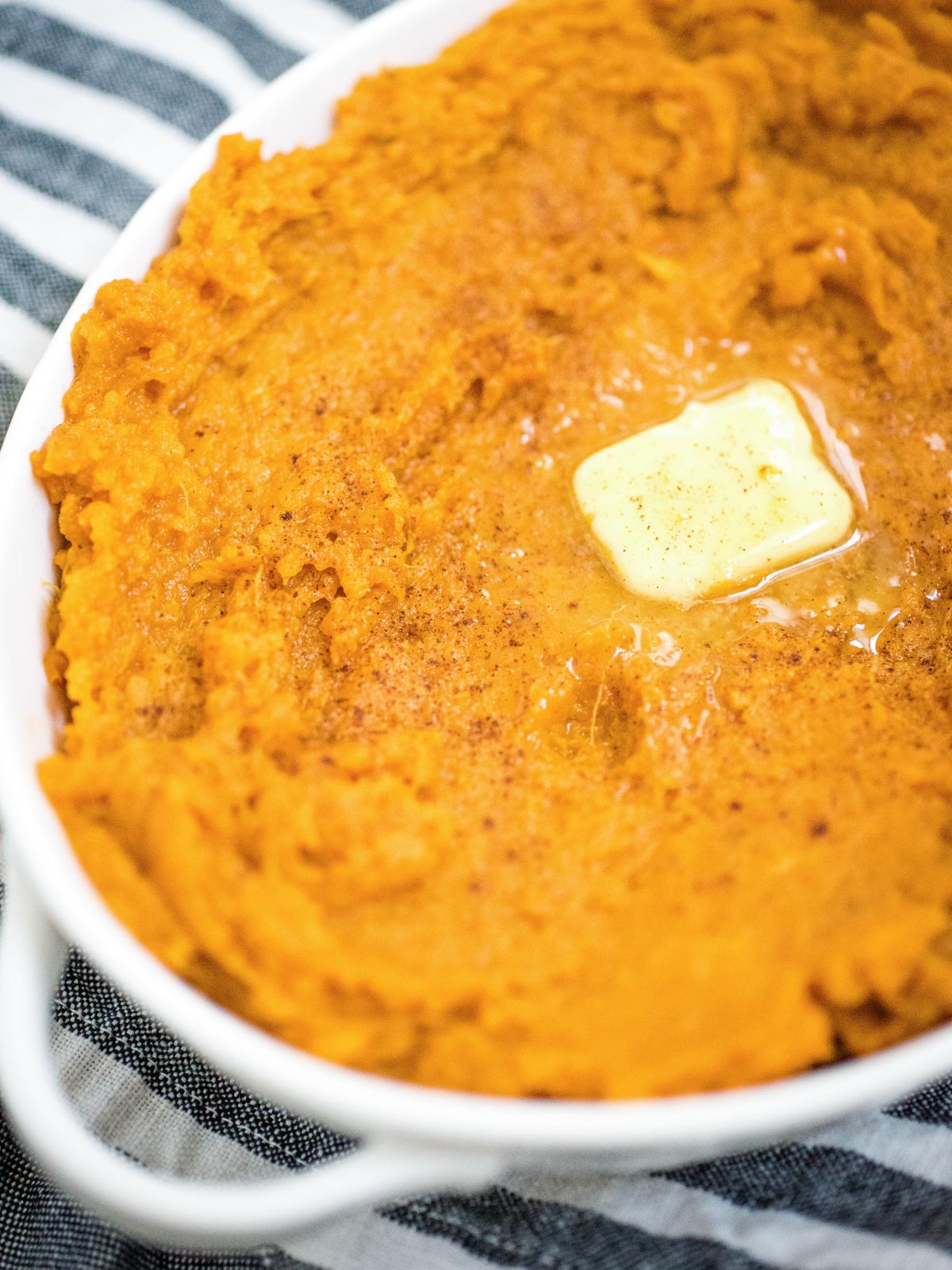 butter melting on top of mashed sweet potatoes in a white baking dish