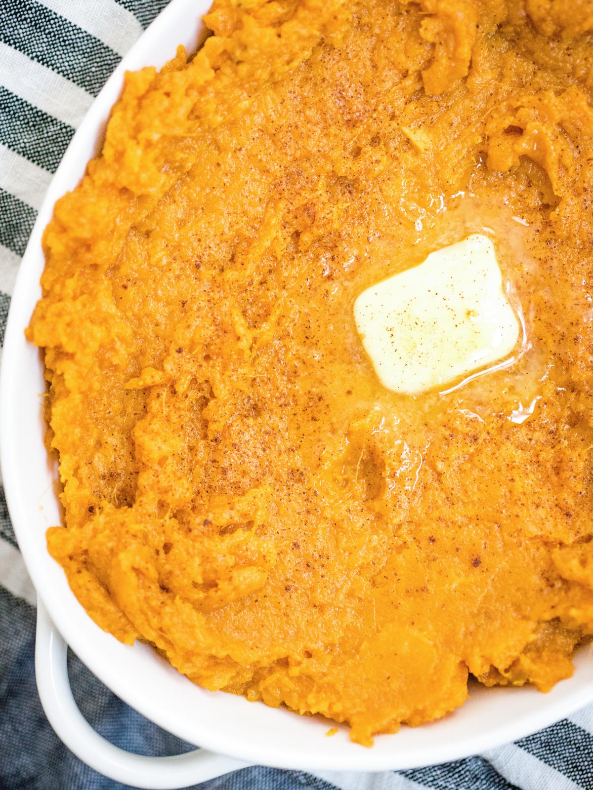 mashed sweet potatoes in a white baking dish topped with butter