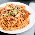 instant pot spaghetti and meat sauce on a white plate topped with parmesan and basil
