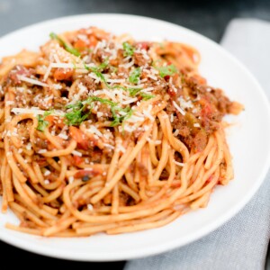 instant pot spaghetti and meat sauce on a white plate topped with parmesan and basil