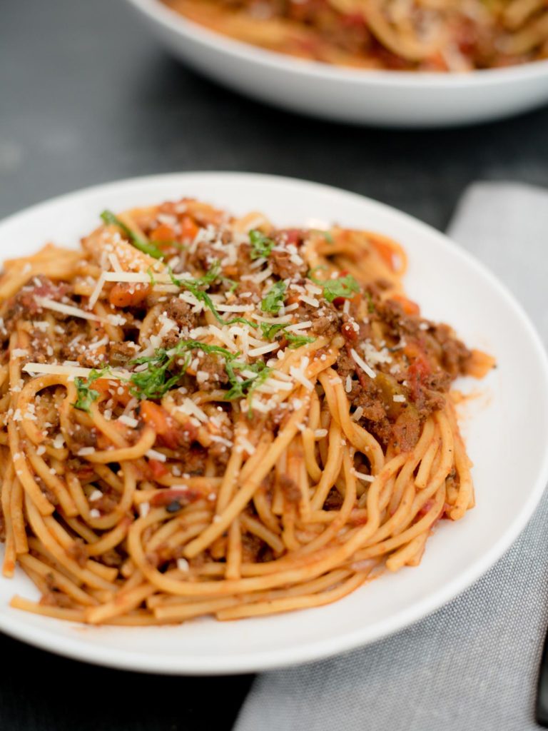instant pot spaghetti and meat sauce on a white plate topped with parmesan and basil