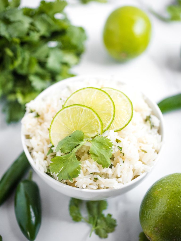 jalapeno lime rice in a white bowl topped with limes and cilantro