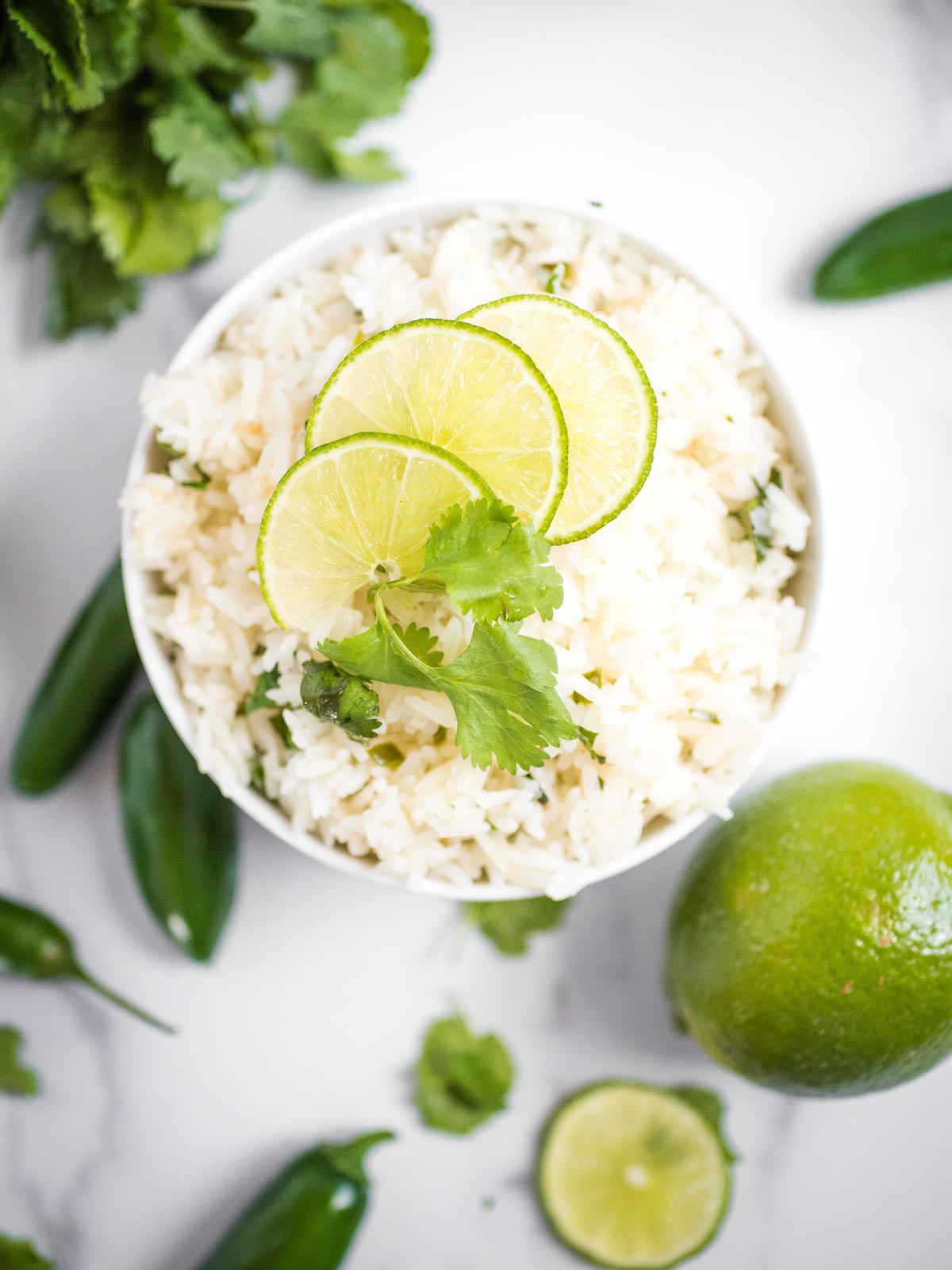 jalapeno lime rice in a white bowl topped with limes and cilantro