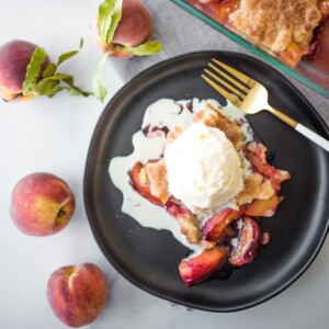 peach cobbler on a black plate topped with ice cream