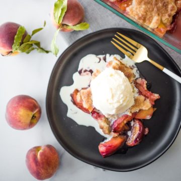 peach cobbler on a black plate topped with ice cream
