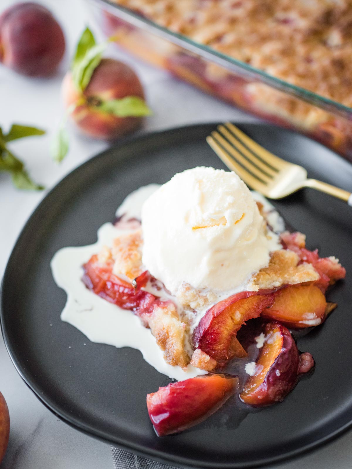 peach cobbler on a black plate topped with ice cream