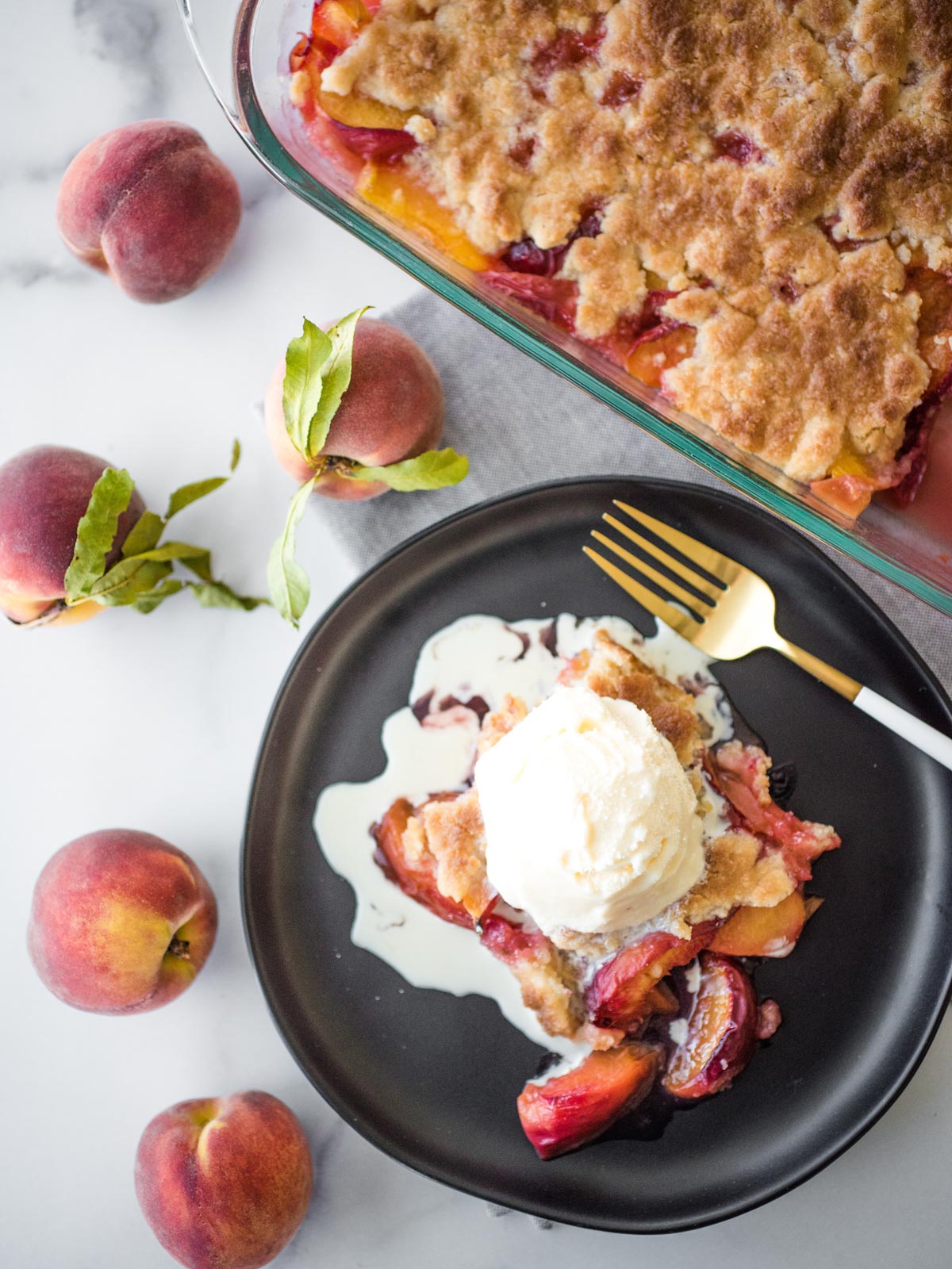 peach cobbler topped with ice cream on a black plate