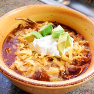Crockpot Mexican Chili in a yellow bowl topped with cheese, sour cream, and avocado