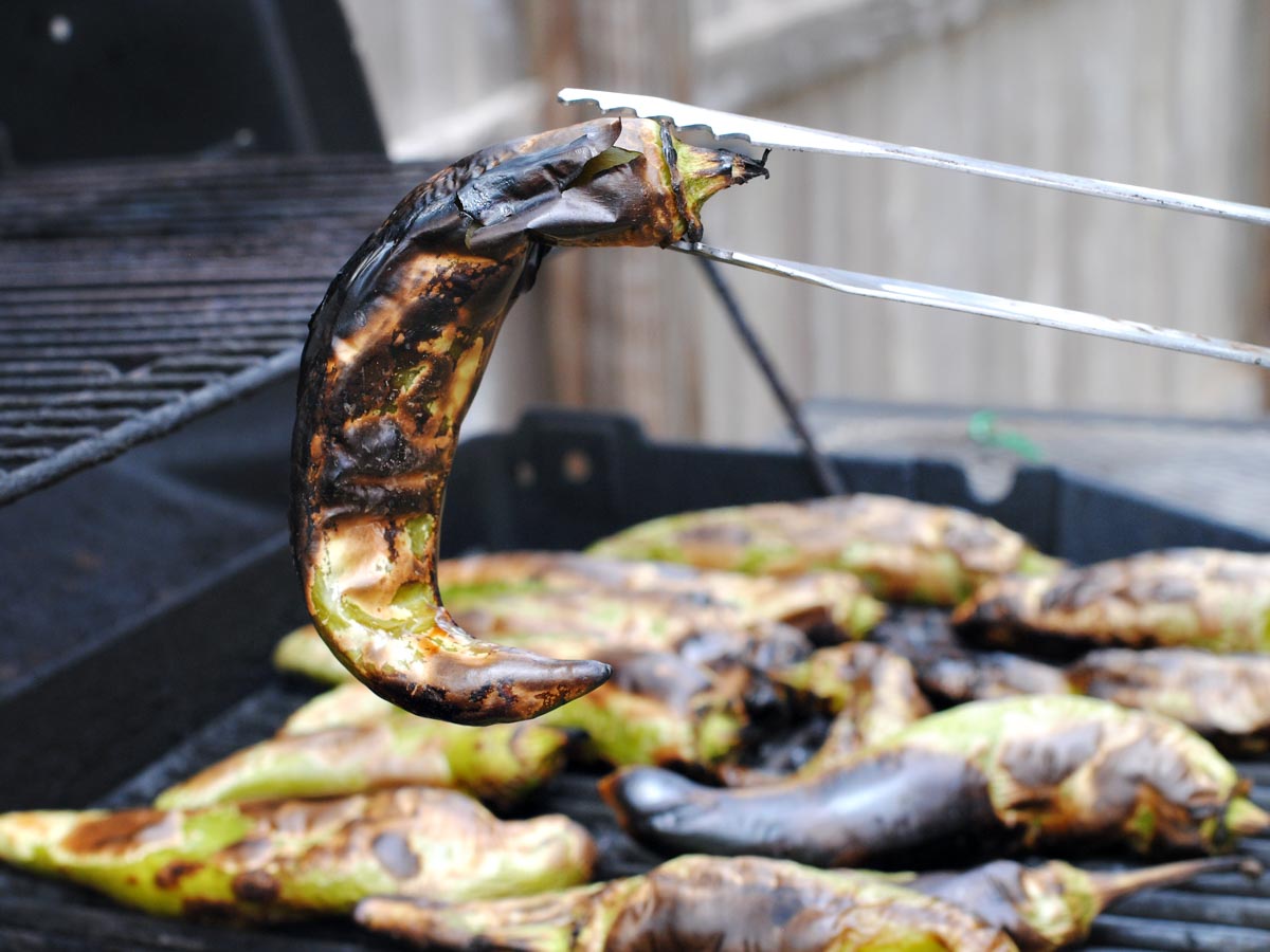 tongs holding up a roasted green chile above a grill