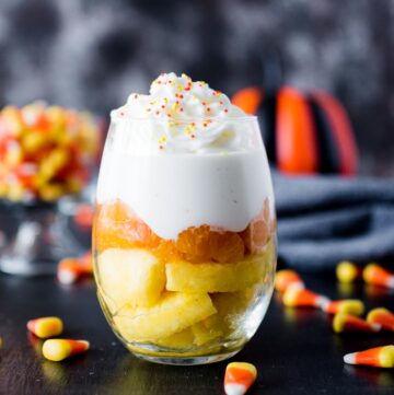 candy corn inspired fruit parfait in a glass surrounded by candy corn