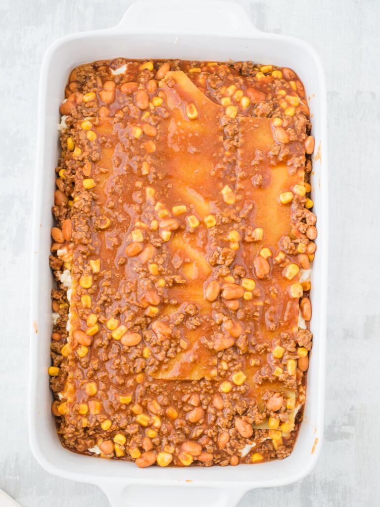 sauce poured on tex mex lasagna in a casserole dish