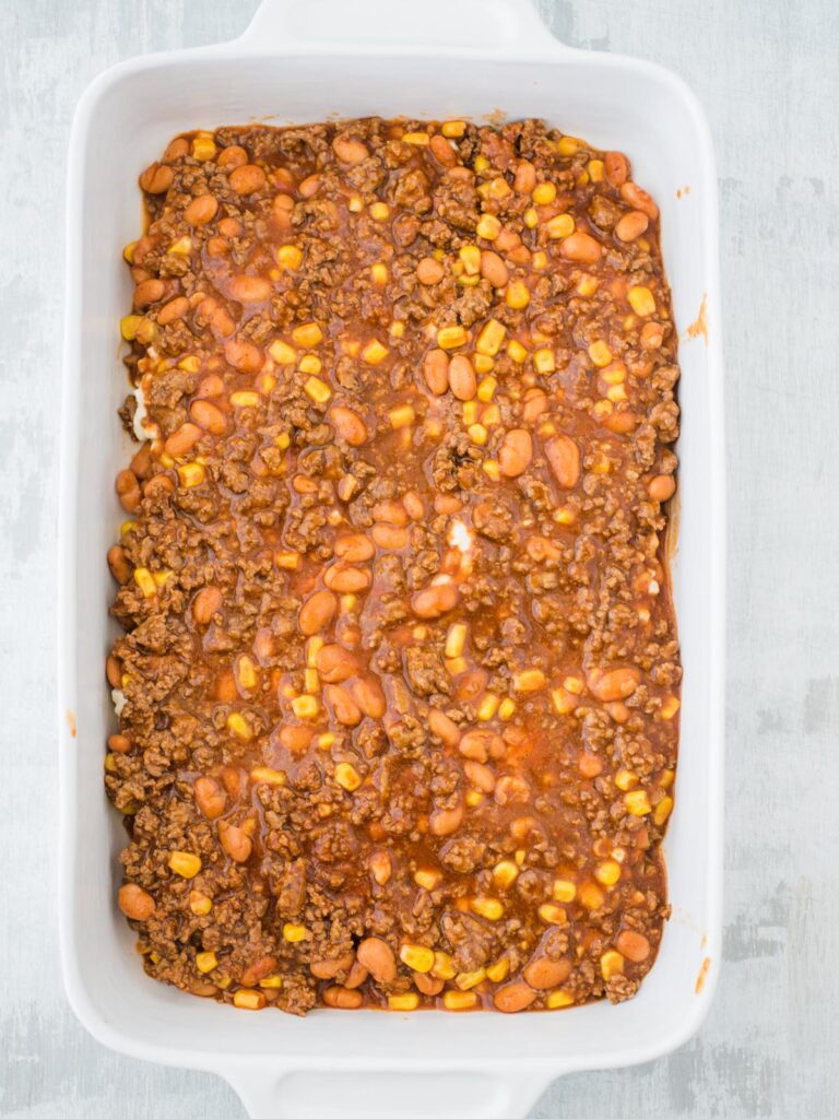 sauce poured on tex mex lasagna in a casserole dish
