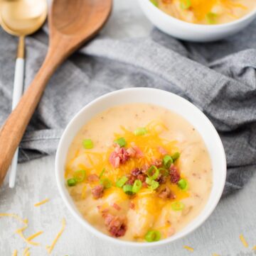 slow cooker potato soup in white bowl with toppings of cheese and scallion