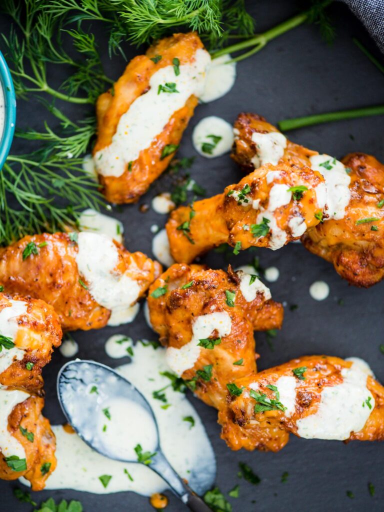 crispy chicken wings in the air fryer sprinkled with parsley and a ranch drizzle