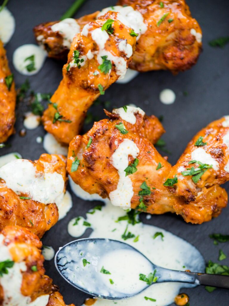 crispy chicken wings in the air fryer sprinkled with parsley and a ranch drizzle