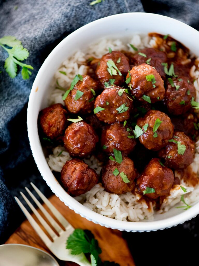 crockpot sweet and spicy meatballs over rice topped with parsley