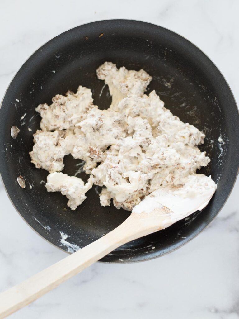 cream cheese and sausage mixed together in a skillet with wooden spoon