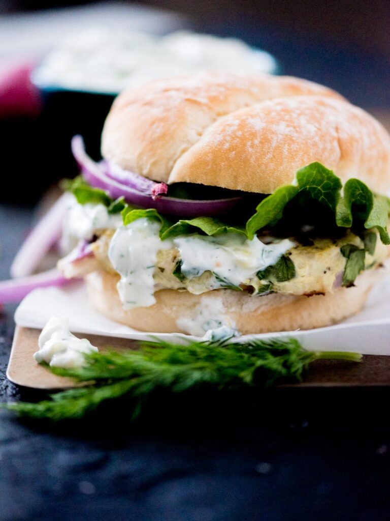 greek turkey burger in a bun topped with tzatziki sauce, red onion, and lettuce