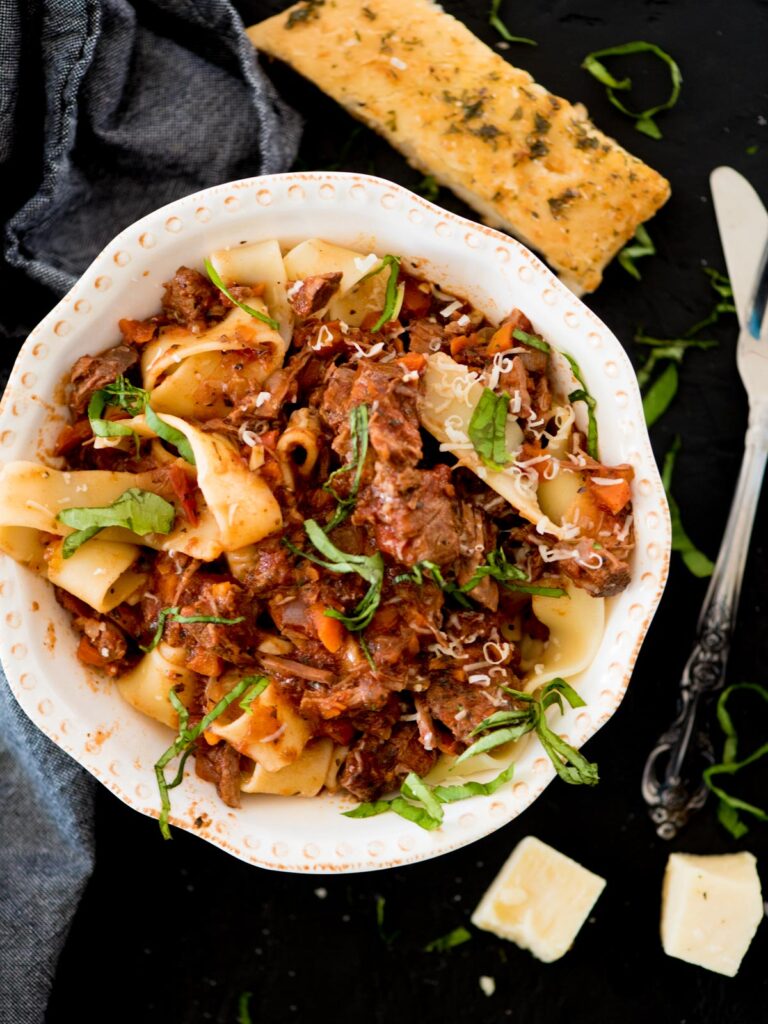 beef ragu over pasta topped with basil and parmesan