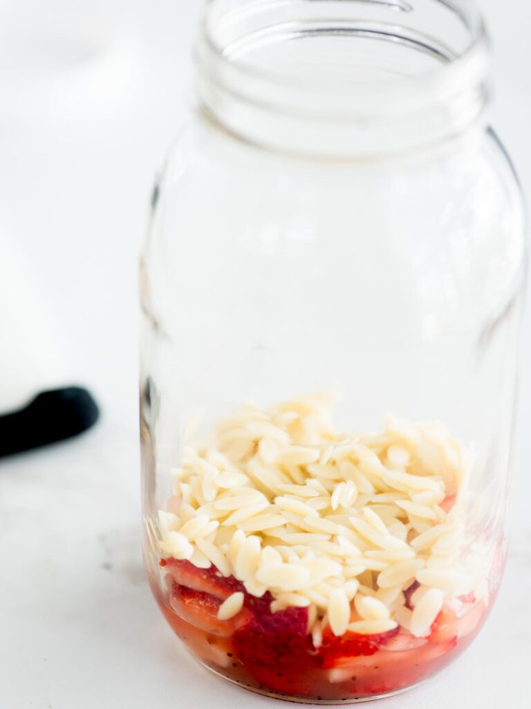 orzo added to mason jar with strawberries and vinaigrette