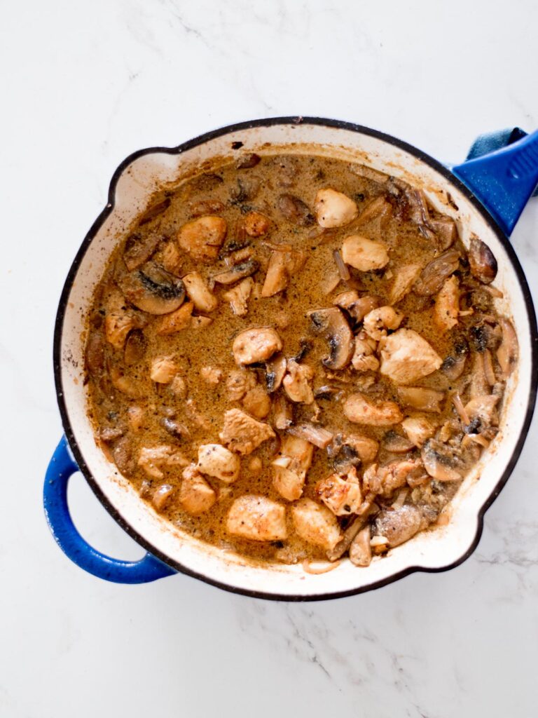 chicken and broth added to a skillet with mushrooms and onion