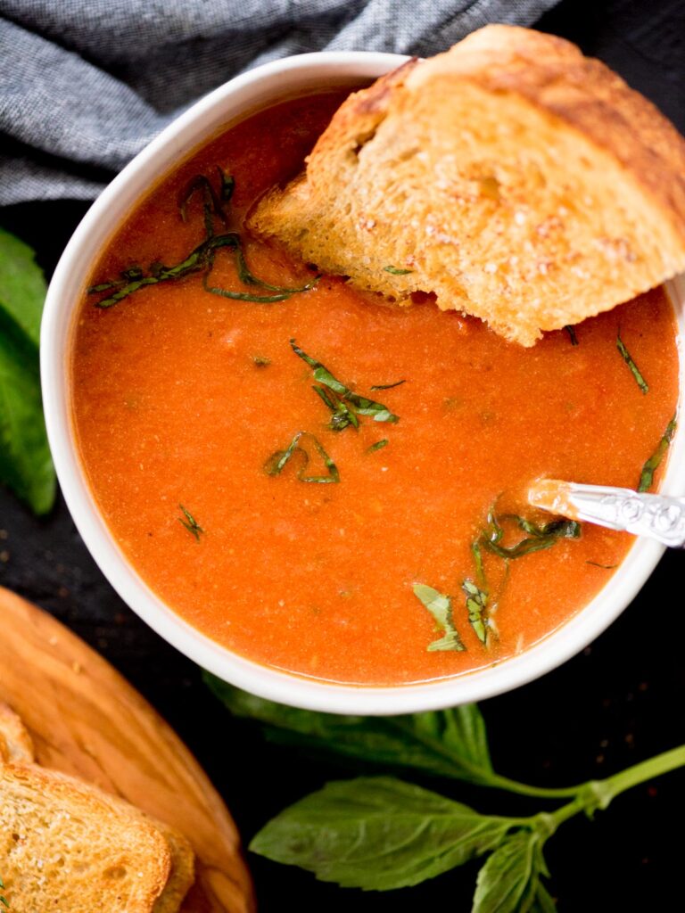 roasted tomato basil soup in a bowl topped with basil and a grilled cheese dipped in