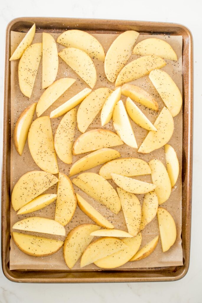seasoned potato wedges on a parchment lined baking sheet with salt and pepper