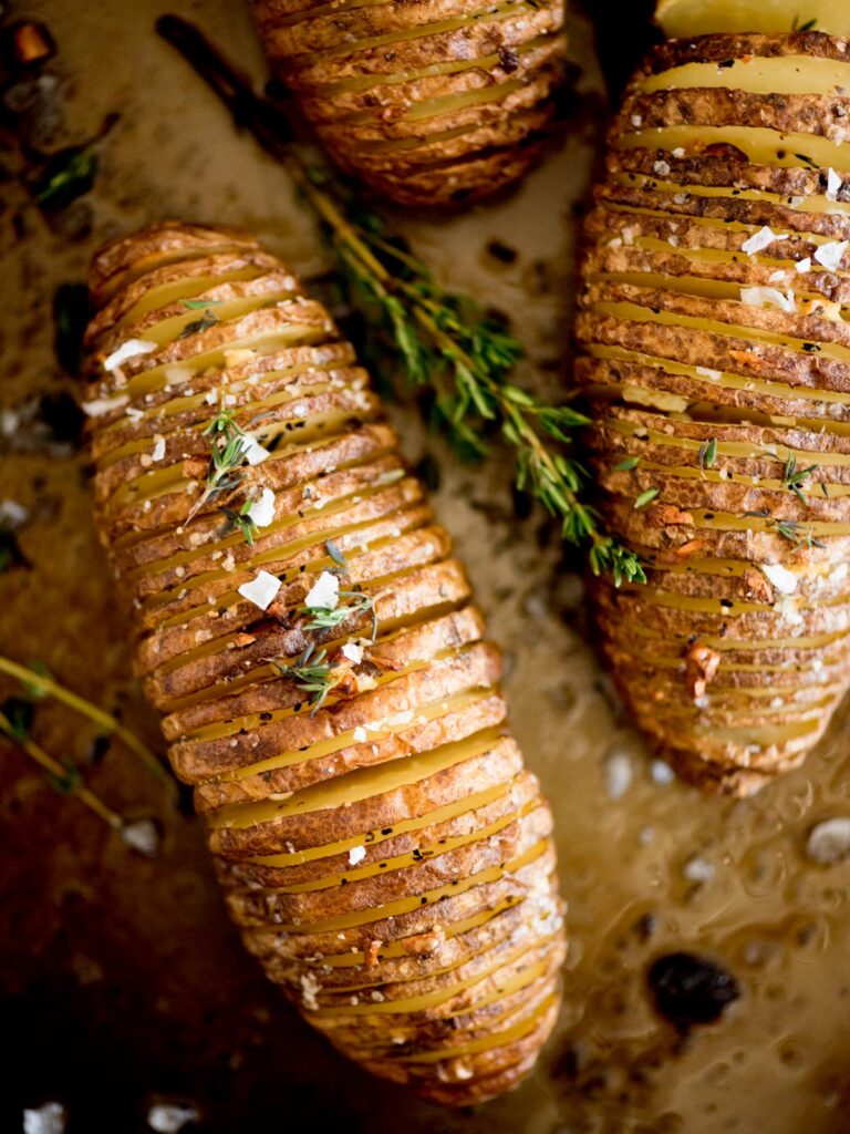 garlic butter hasselback potatoes topped with fresh thyme and flaked salt
