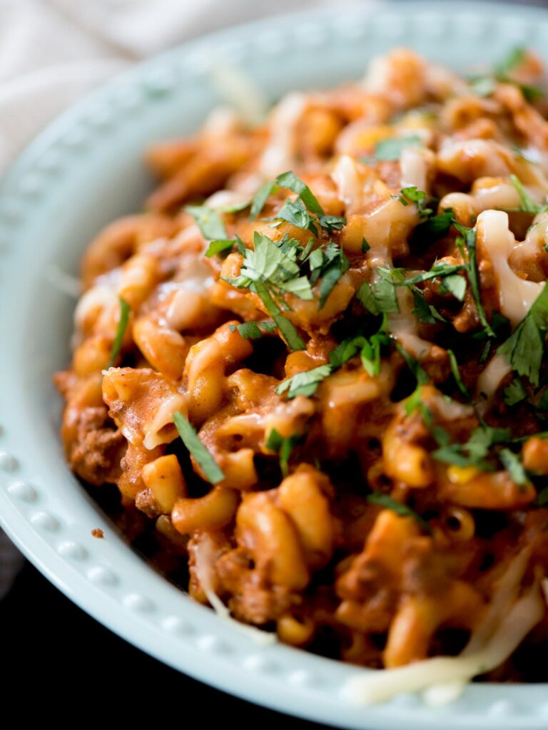 one pot cheesy taco pasta in a blue bowl topped with cheese and cilantro